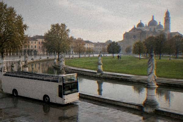 A plain open-top tour bus without markings parked beside the green ring canal of a huge elliptical square, plane trees and weathered stone figures along the water, Prato della Valle
