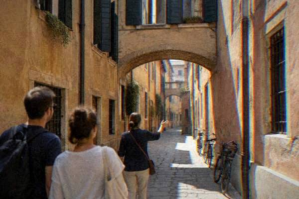 A guide and a couple standing in a narrow lane of ochre houses beneath a low stone arch, shutters open above, Jewish Ghetto
