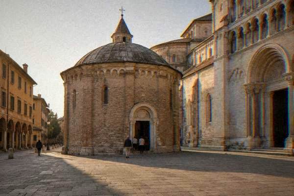A few visitors small in the frame at the doorway of a small Romanesque brick baptistery with a low dome beside a pale cathedral, Baptistery of Padua
