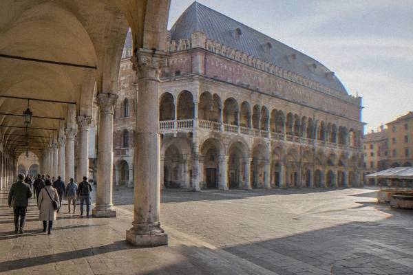 A small walking group following a guide along the long arcade of a great medieval hall between two market squares, Palazzo della Ragione