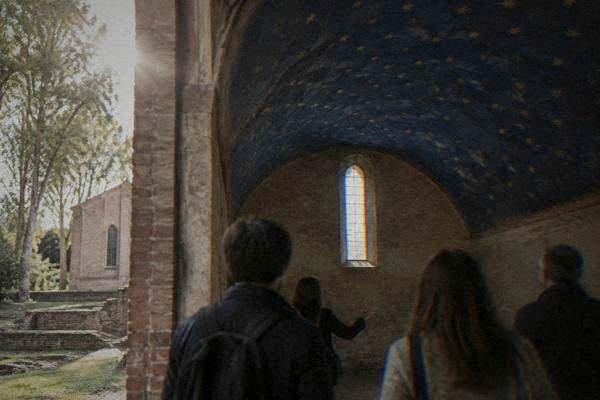 A guide and a few visitors seen from behind in a small barrel-vaulted room with a deep blue ceiling dotted with small gold stars, Scrovegni Chapel