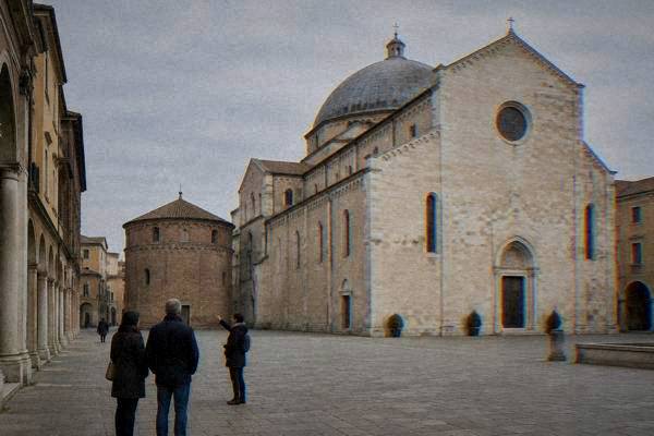 A local guide and a couple pausing on a quiet square before a plain pale stone cathedral with a big low dome, Padua Cathedral