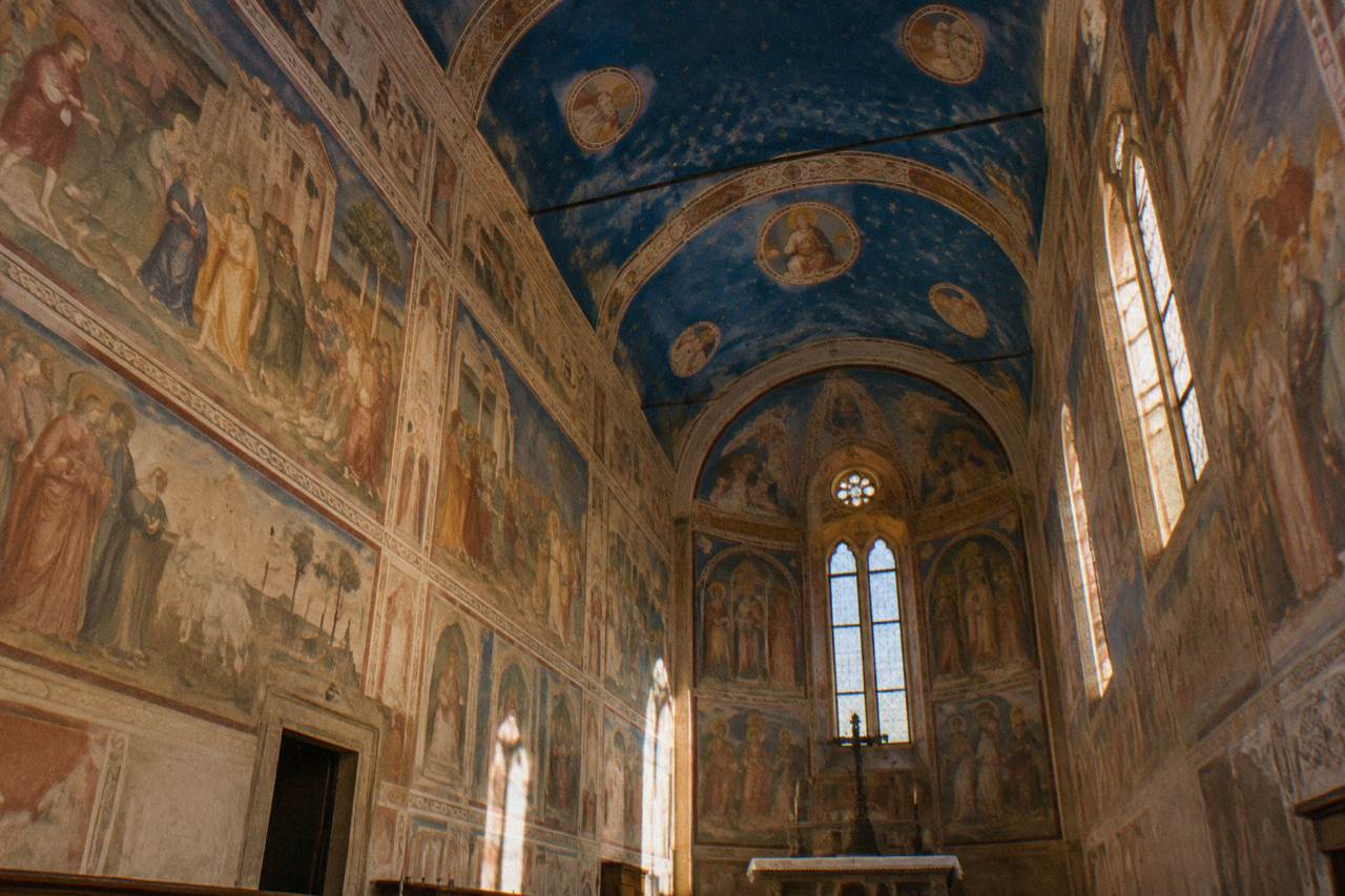 The frescoed interior of a small chapel in Padua with blue-painted vaults and narrative scenes along the walls