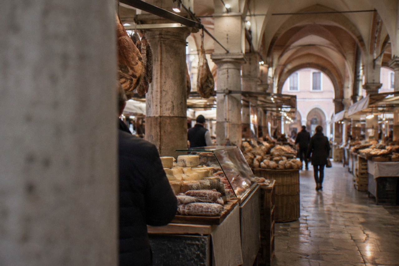 A covered food market hall in Padua with stalls of cheese, cured meats and bread under vaulted ceilings