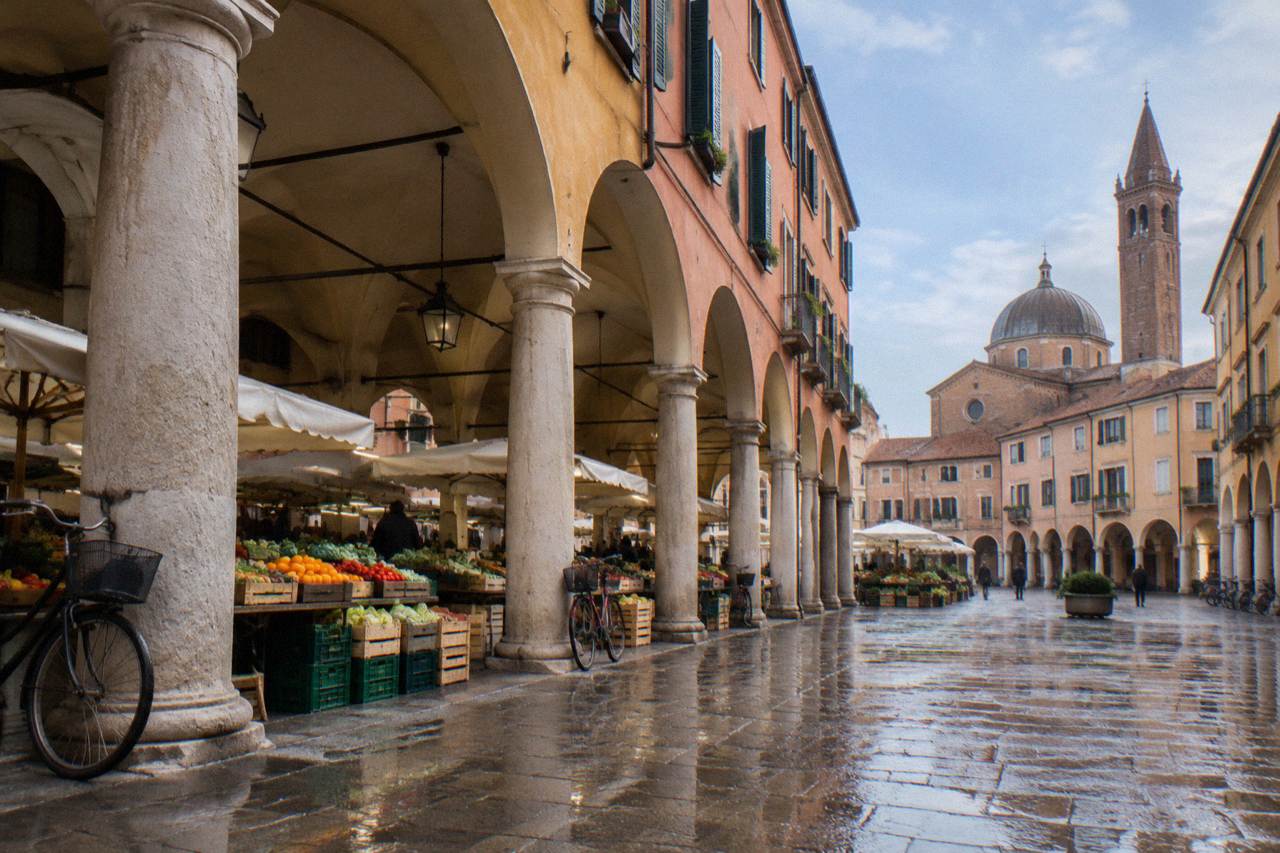 Market stalls with crates of fresh fruit and vegetables under the arcades of a Padua square