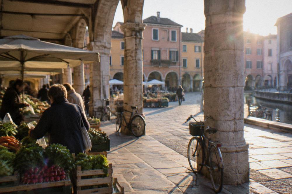 Shoppers at an outdoor vegetable market under the arcades of a Padua square