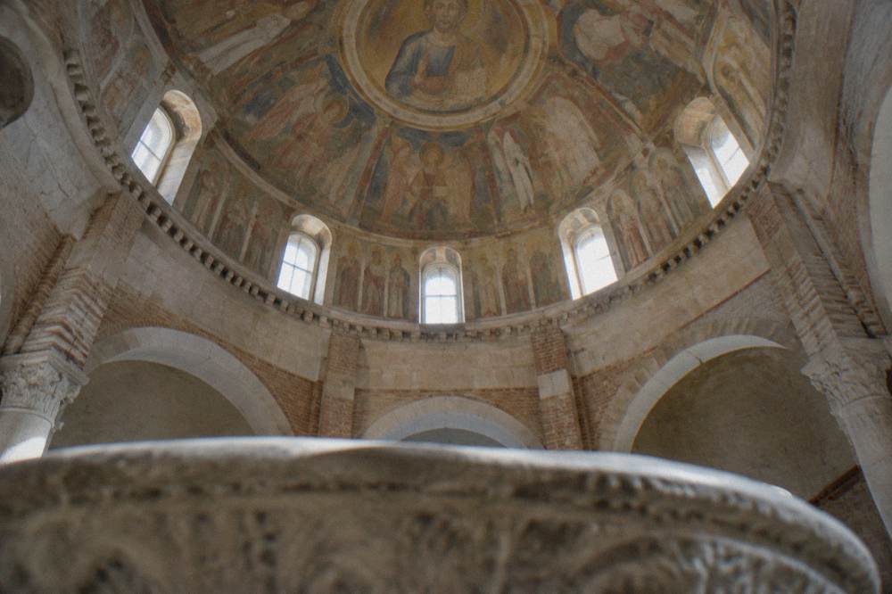 The frescoed interior of an Italian baptistery with a domed ceiling