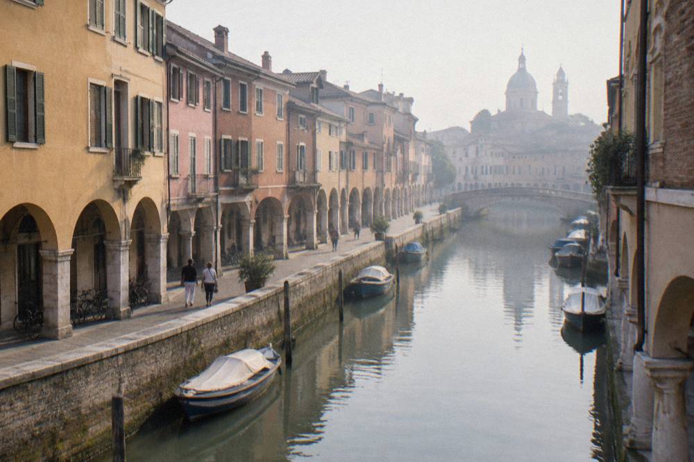 A narrow canal with stone embankments and moored small boats in Padua