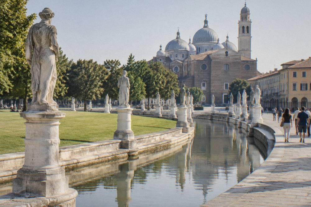 People strolling beside the statue-lined canal of Prato della Valle with the Basilica of Santa Giustina behind