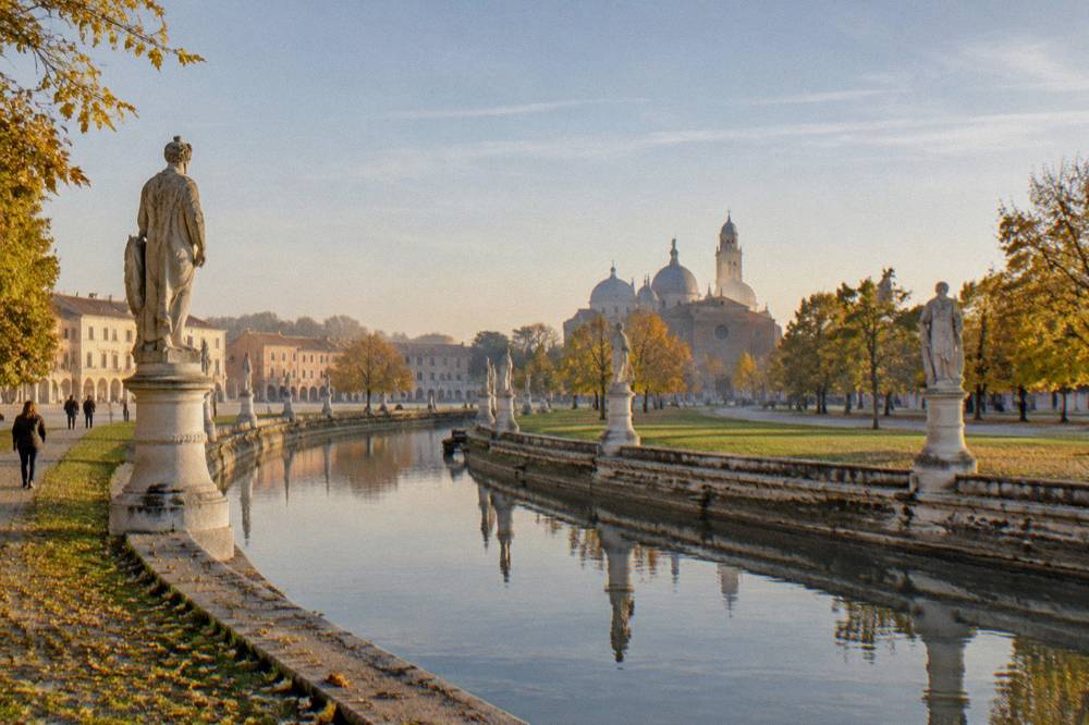 Autumn light on the statue-lined canal of Prato della Valle in Padua with leaves on the ground
