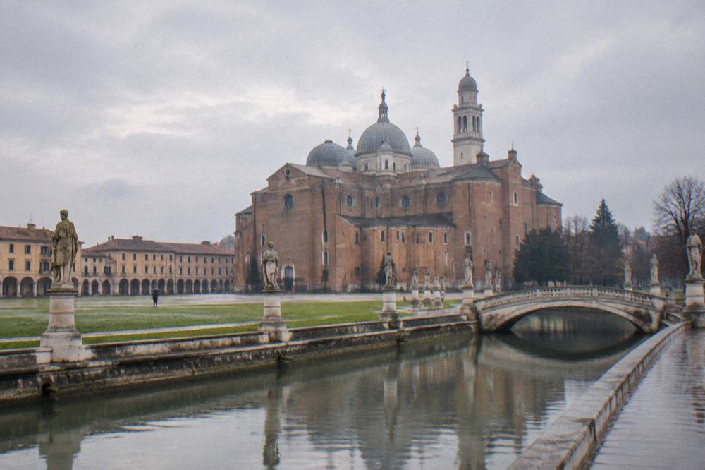 A stone bridge over a canal toward a park island, with rows of statues along the water