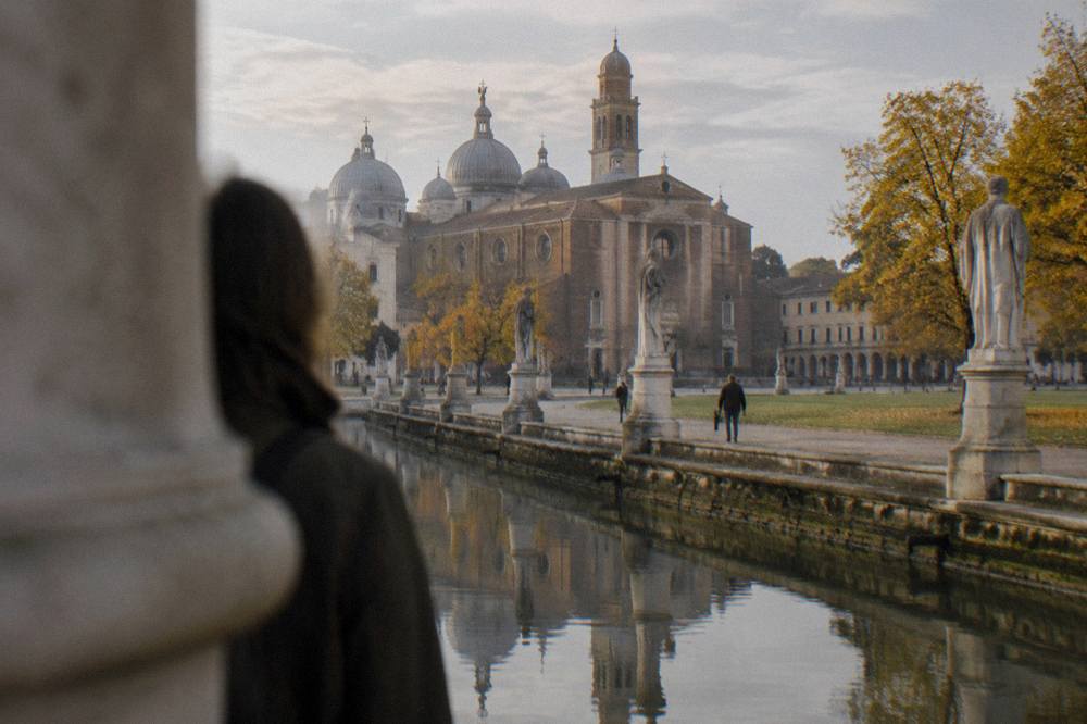 Statues reflected in a canal under autumn clouds around a large city square