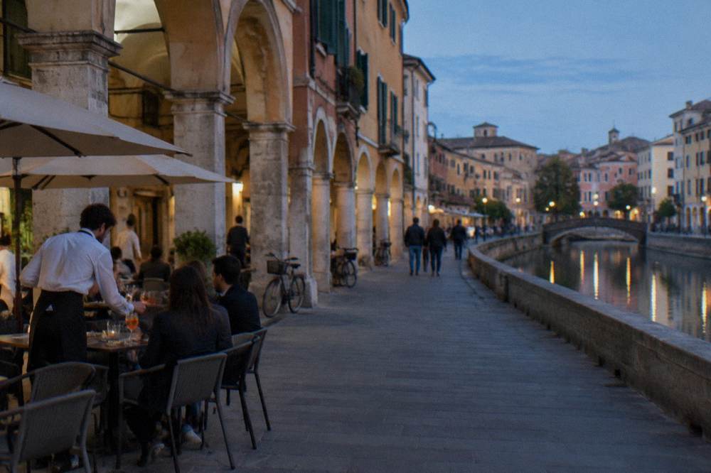 Waiters serving drinks at outdoor tables beside a historic arcade in Padua