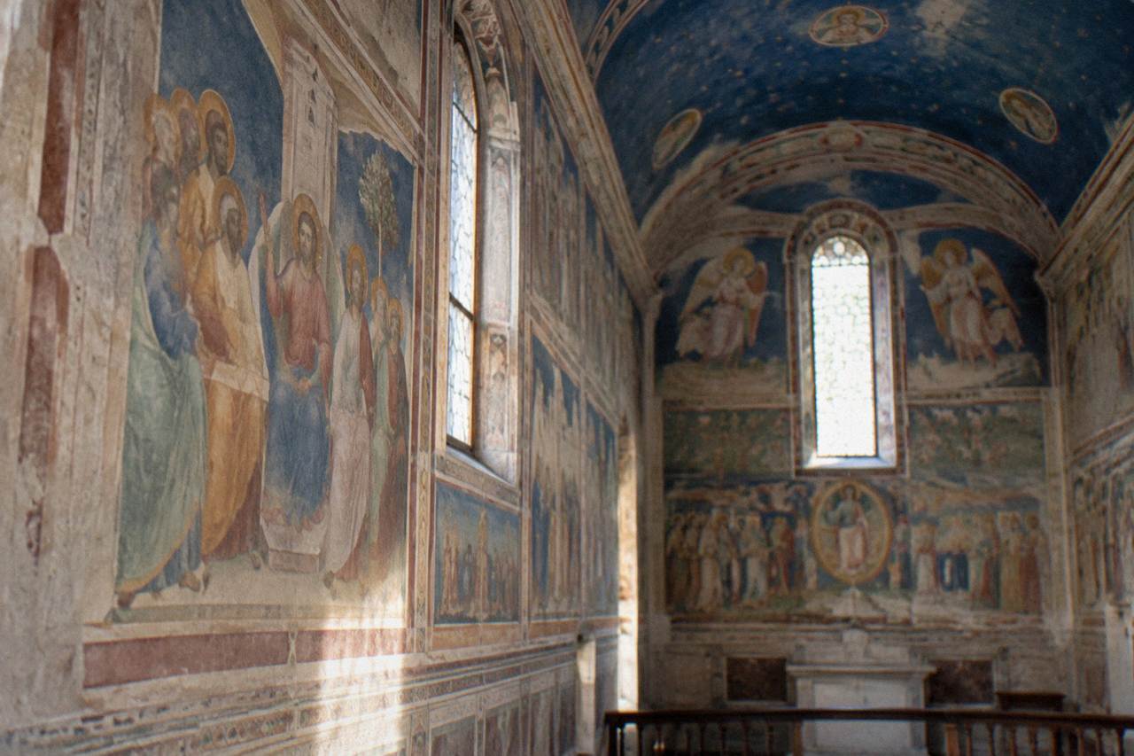 Frescoed interior wall of a small medieval chapel with blue painted ceilings and narrative scenes