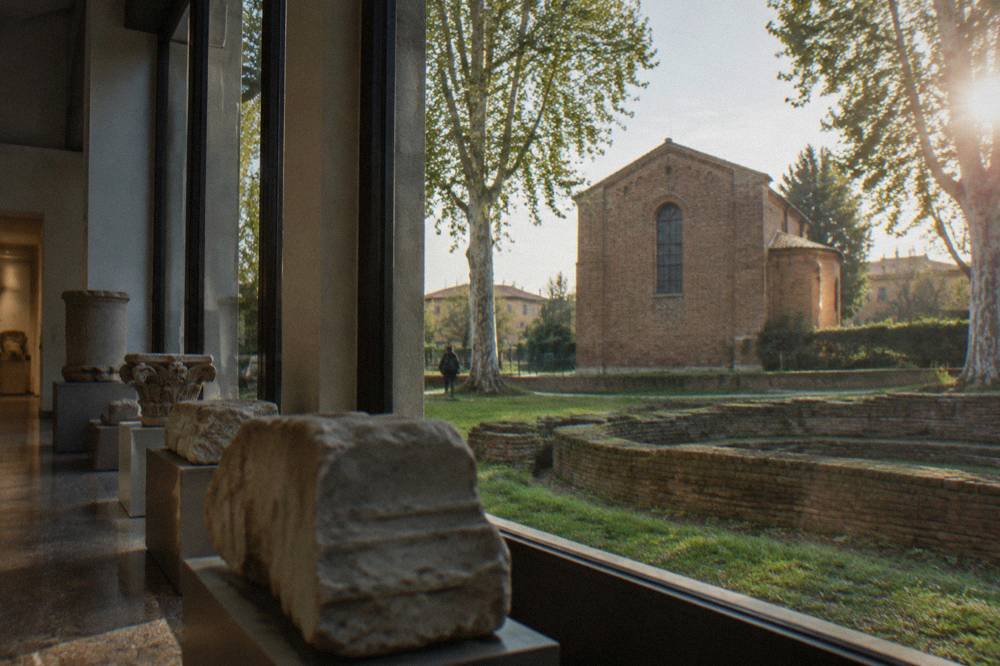 Museum gallery with archaeological stone fragments displayed beside tall windows