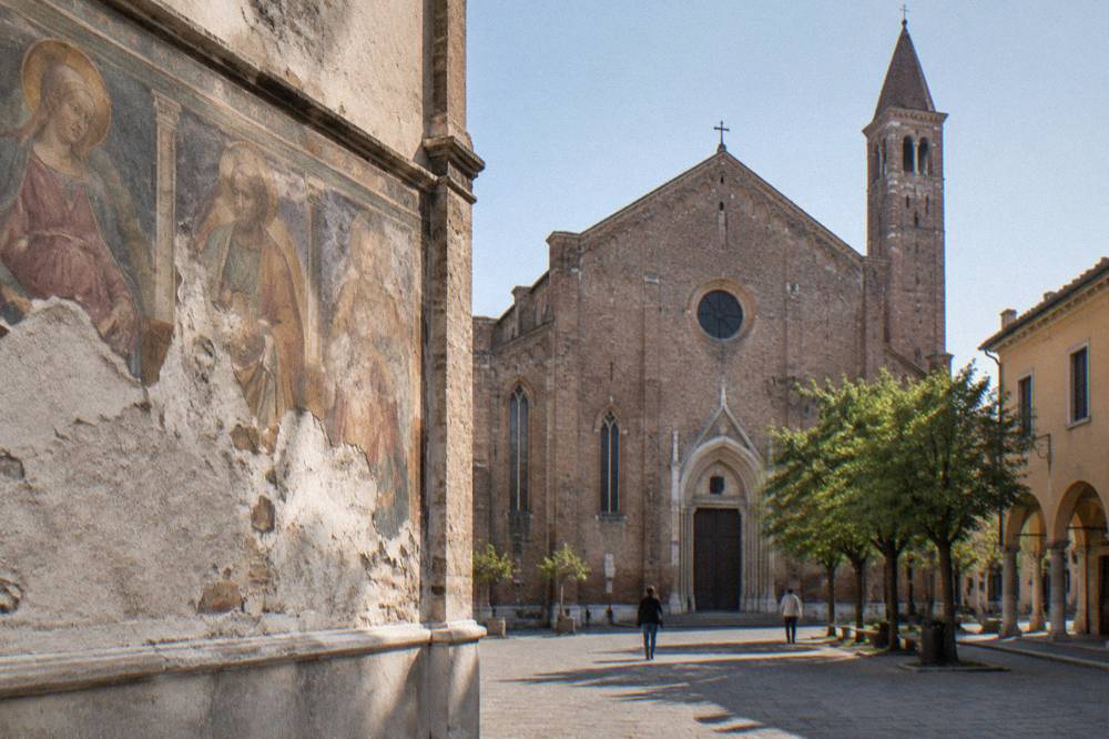 A frescoed chapel wall with damaged plaster showing surviving painted figures in muted Renaissance colours