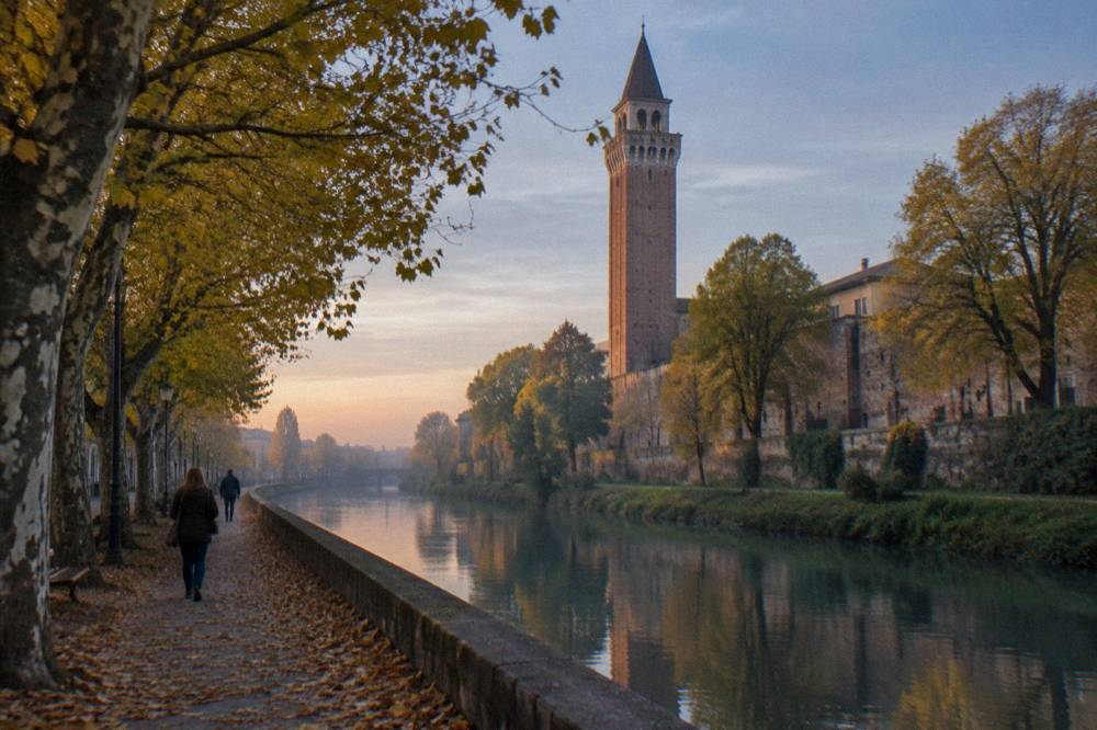 Autumn trees along a canal embankment with fallen leaves on the path and a tower behind