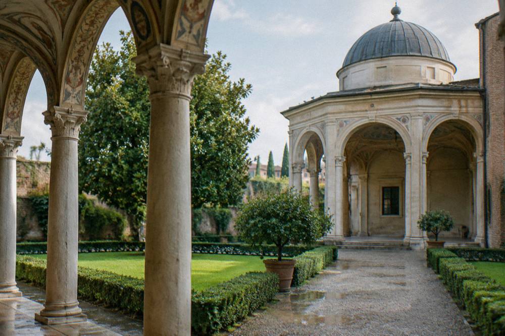 Arched loggia columns with painted decoration above, seen from a garden path