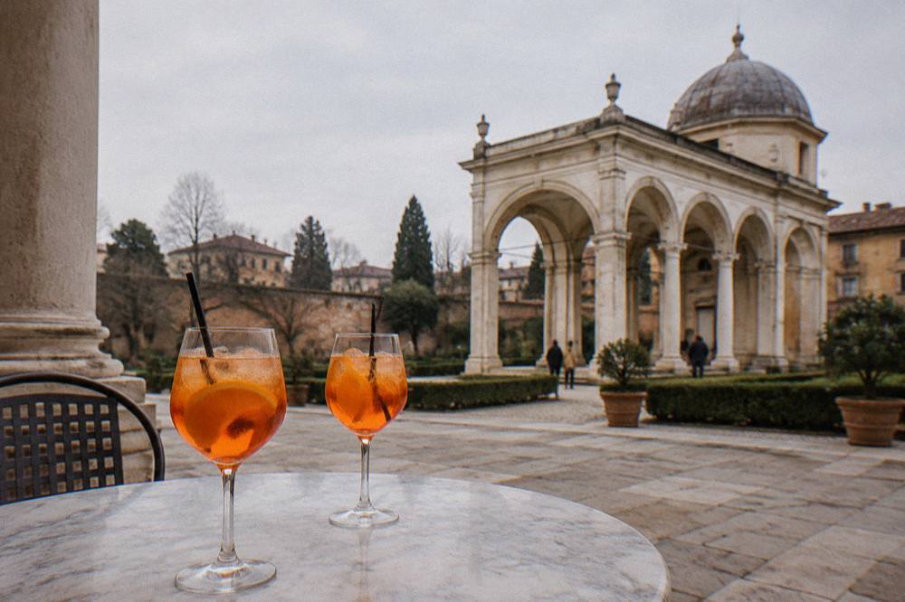 Two spritz cocktails on a marble table in an arcaded square