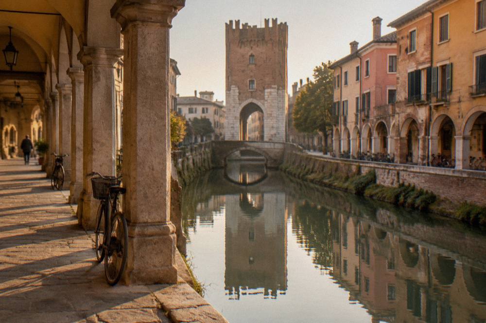 A stone gate tower of the old Padua walls reflected in the canal below it