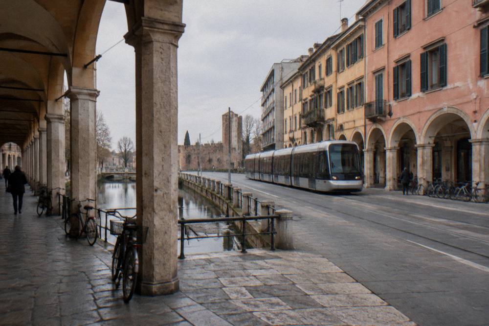 A tram passing modern buildings near the old wall line in Padua