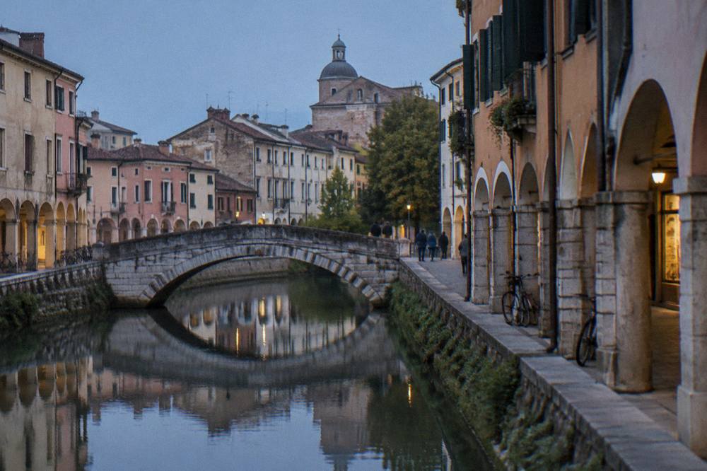 A canal in Padua with an old stone bridge and reflected buildings