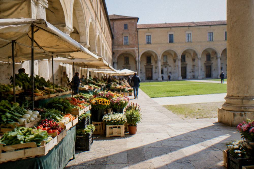 Market stalls with vegetables and flowers under the arcades of an old Paduan square