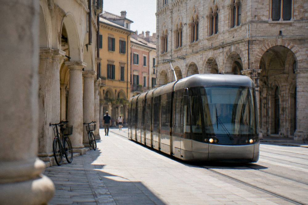 A modern tram passing a historic stone building on a Padua street