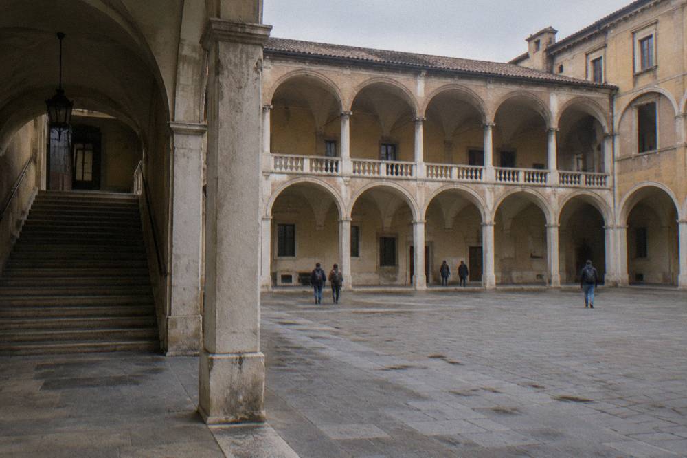 A stone statue of a robed scholar inside a colonnaded courtyard at Palazzo Bo