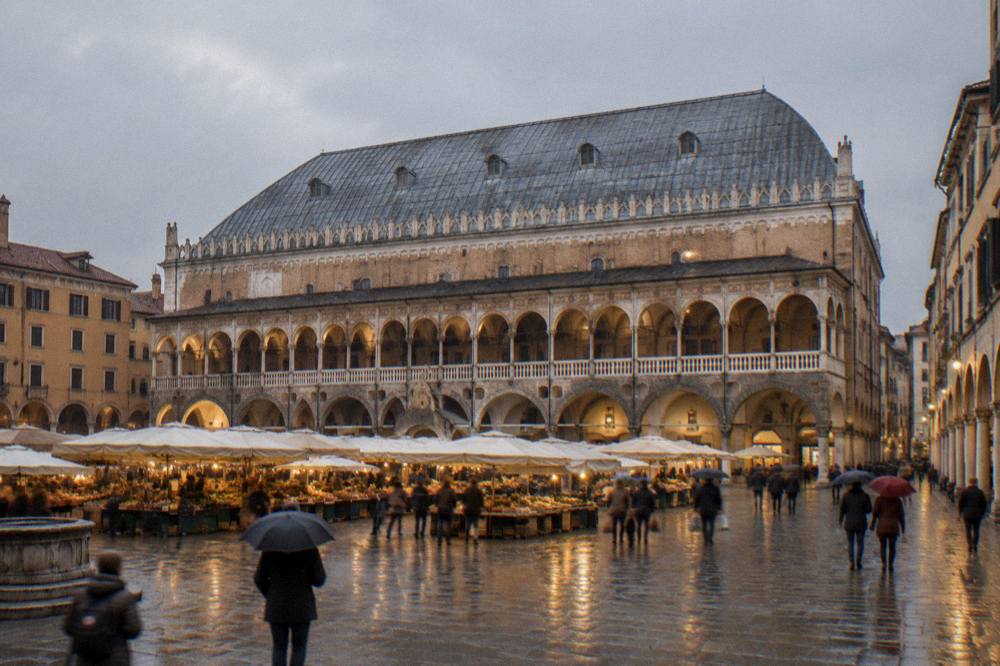 Wide view of the Piazza delle Erbe at dusk with the roofline of the Palazzo della Ragione above the market square
