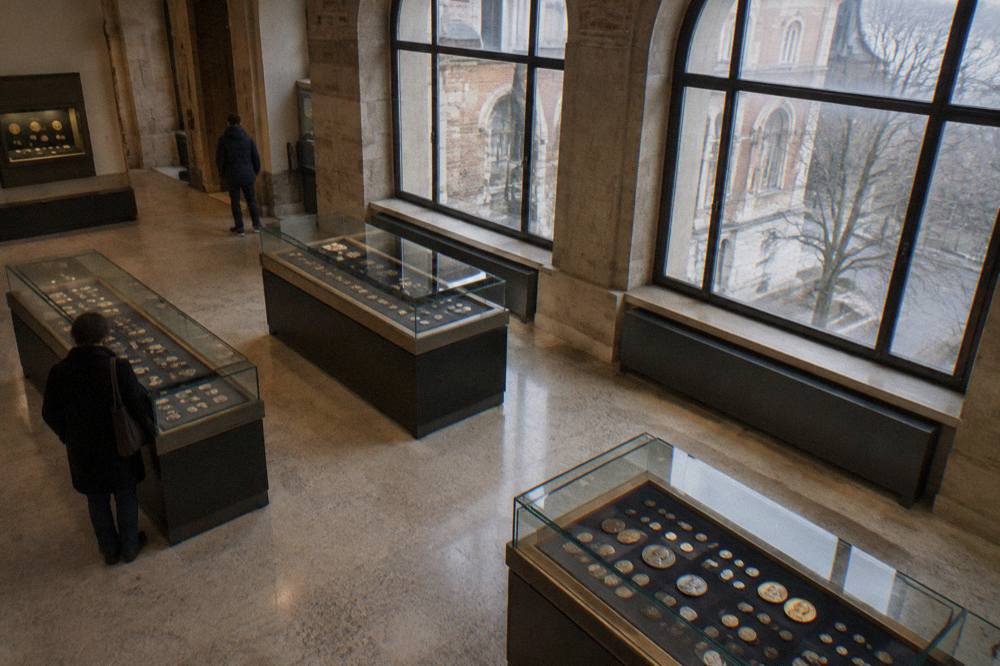 Display cases with antique coins and medals arranged on dark fabric in a museum gallery