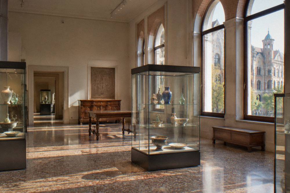 A museum gallery with glass cabinets of decorative objects and wooden furniture under soft lighting