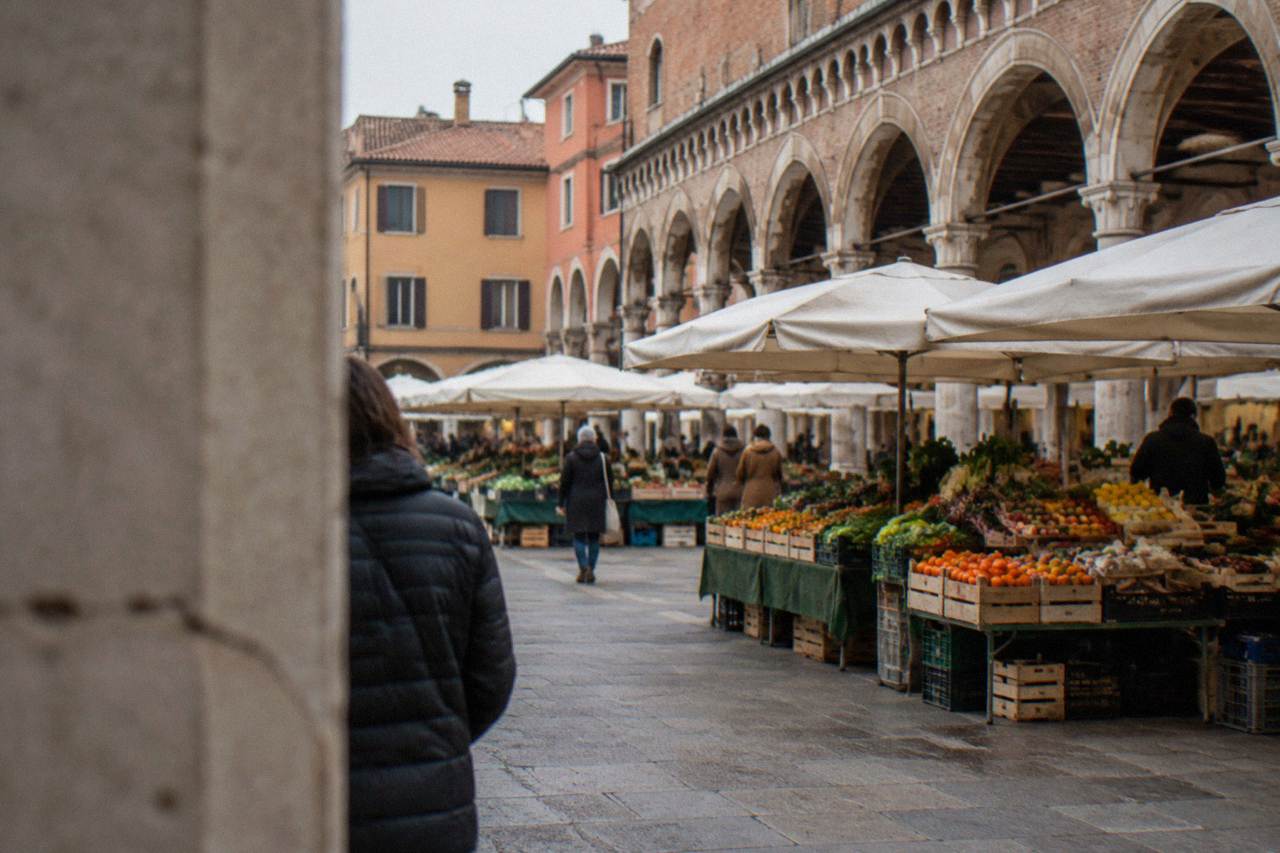 Market stalls with fruit and vegetables under the arcades of an old Italian square