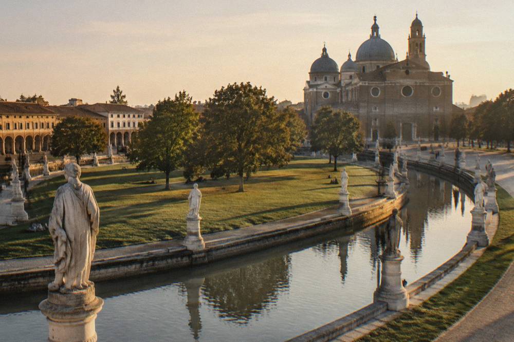 The dome and facade of a large basilica behind the statue-lined canal of an oval square