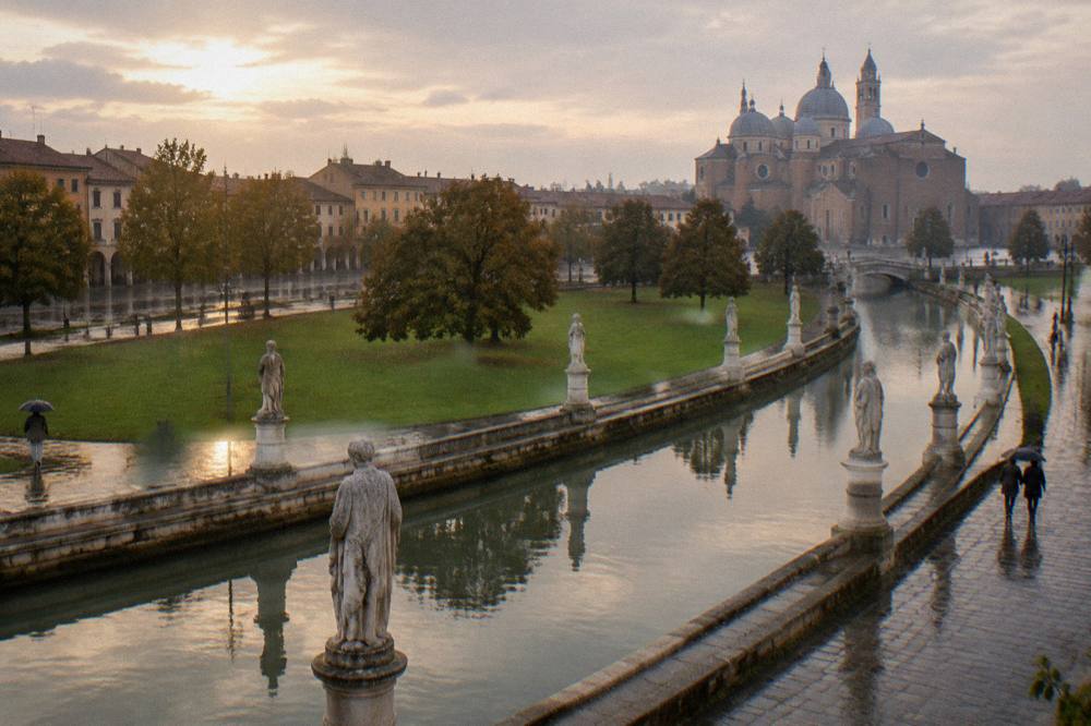 Evening light across a canal and statue pedestals in a large oval square