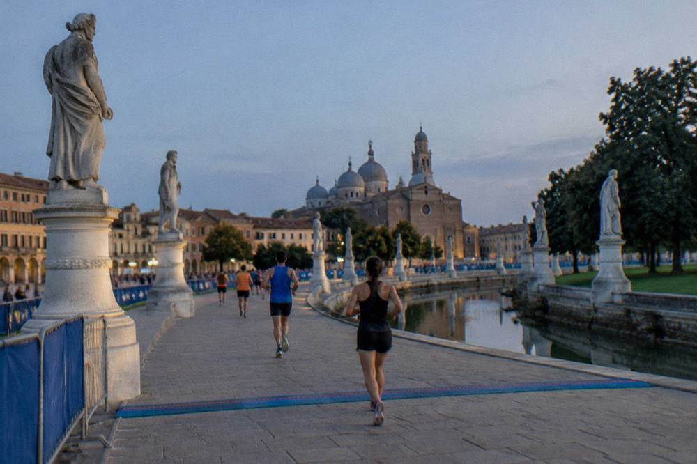 Runners crossing a finish line area in a wide oval square lined with statues