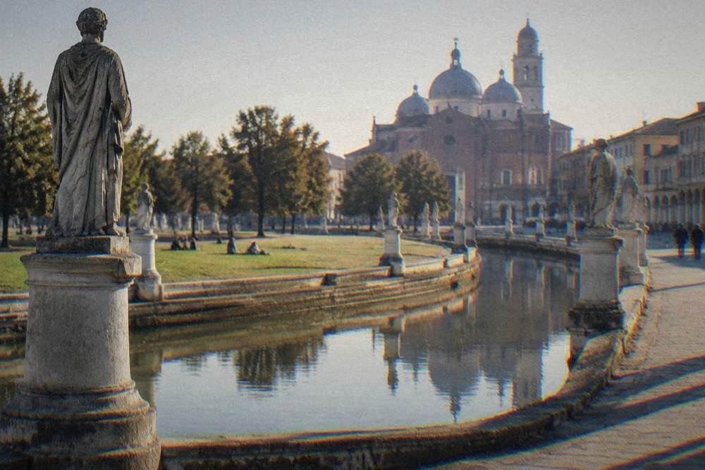Wide elliptical square ringed by a canal and rows of stone statues at dusk