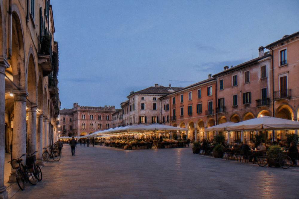 An arcaded square in Padua with market awnings and café tables under old buildings