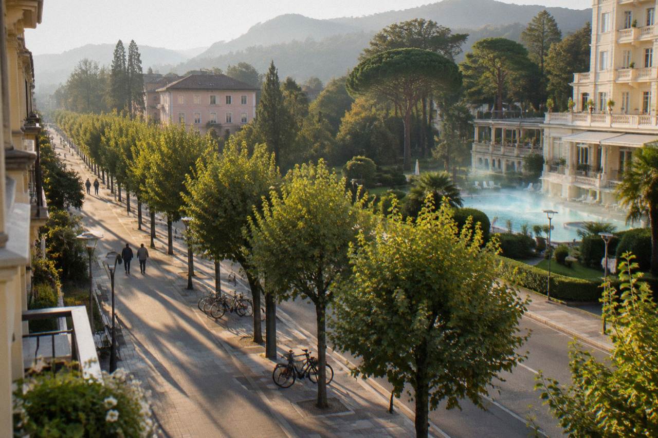 Tree-lined promenade of a small Italian spa town with pastel buildings and parked bicycles