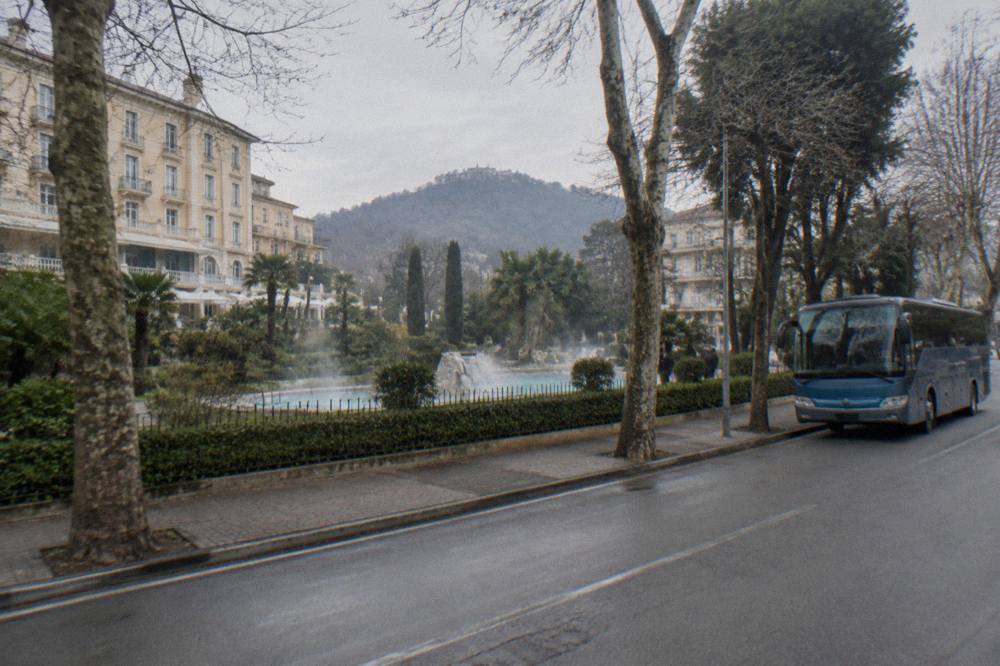 Regional bus parked at a stop outside a thermal town's tree-lined street