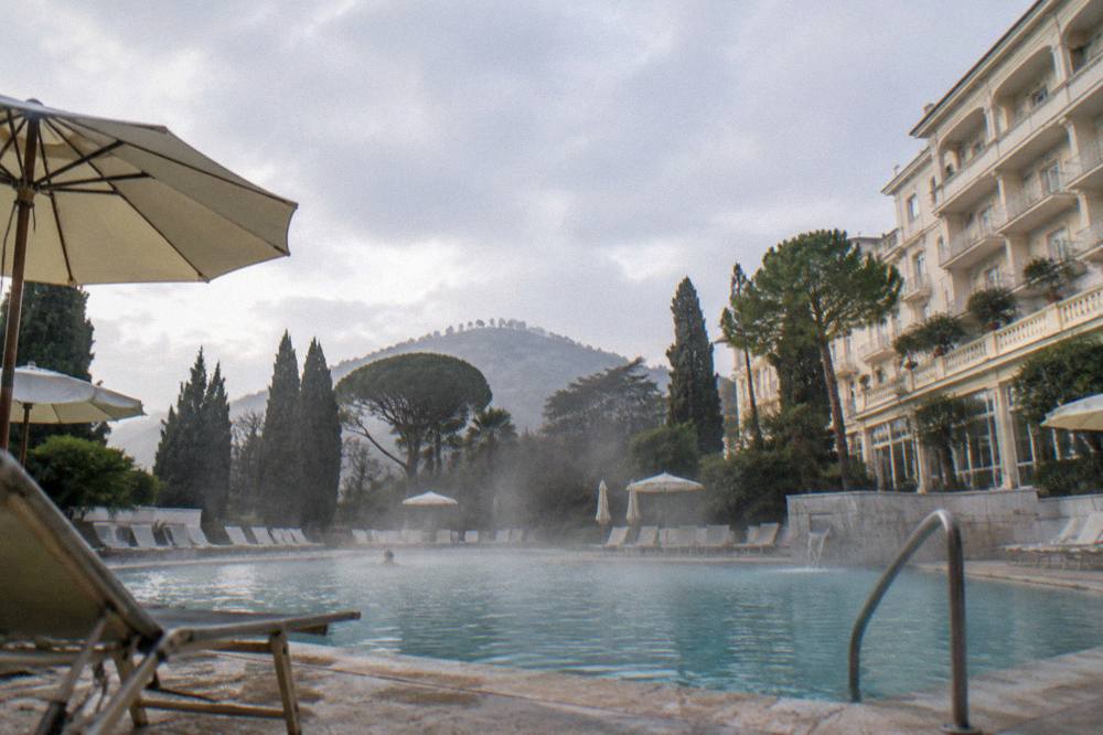 Outdoor thermal pool with steam rising, framed by parasols and lounge chairs