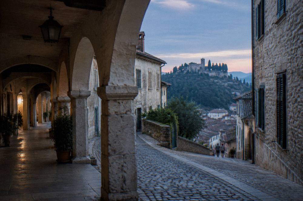 A narrow arcaded street in a Veneto hill town with old stone buildings and shuttered windows