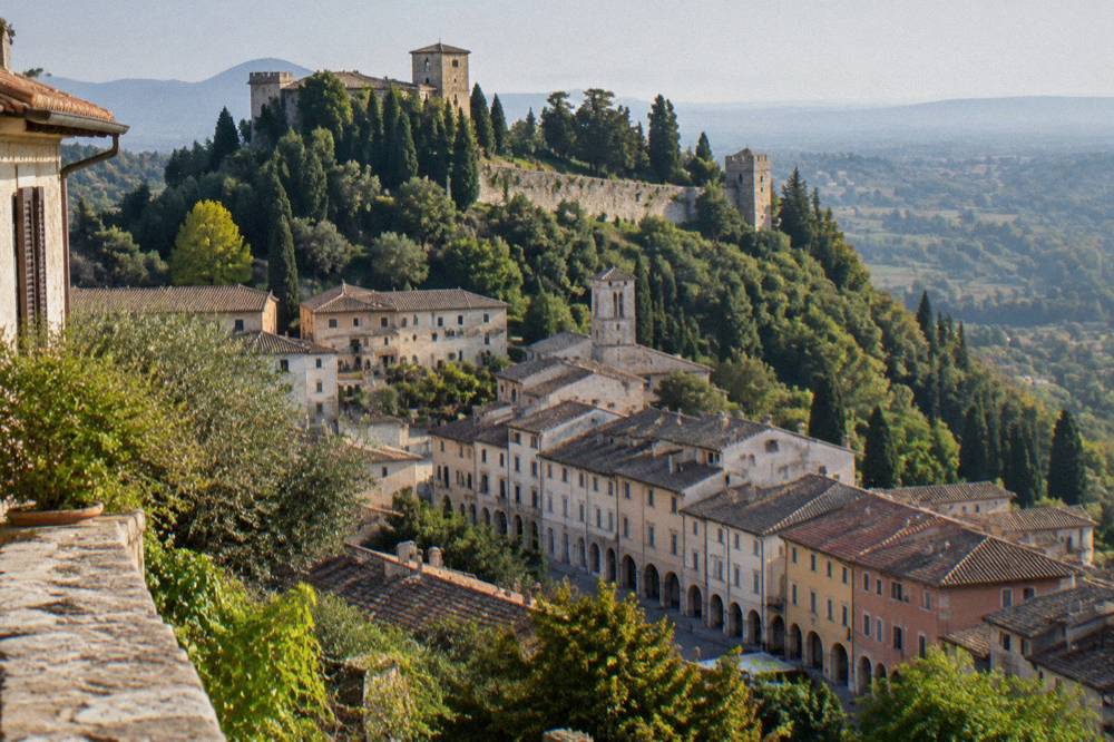The stone fortification walls on a wooded ridge above a small Italian hill town
