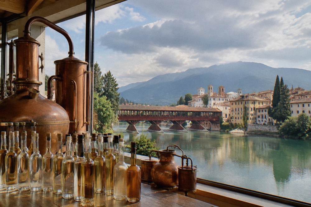 Rows of glass grappa bottles and copper stills inside a distillery