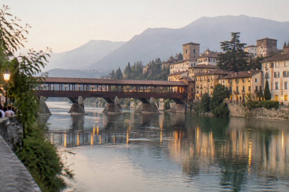 A mountain town at dusk with a lit bridge spanning a river below