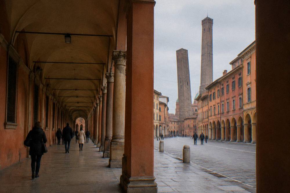 People walking under a long portico in Bologna in soft evening light