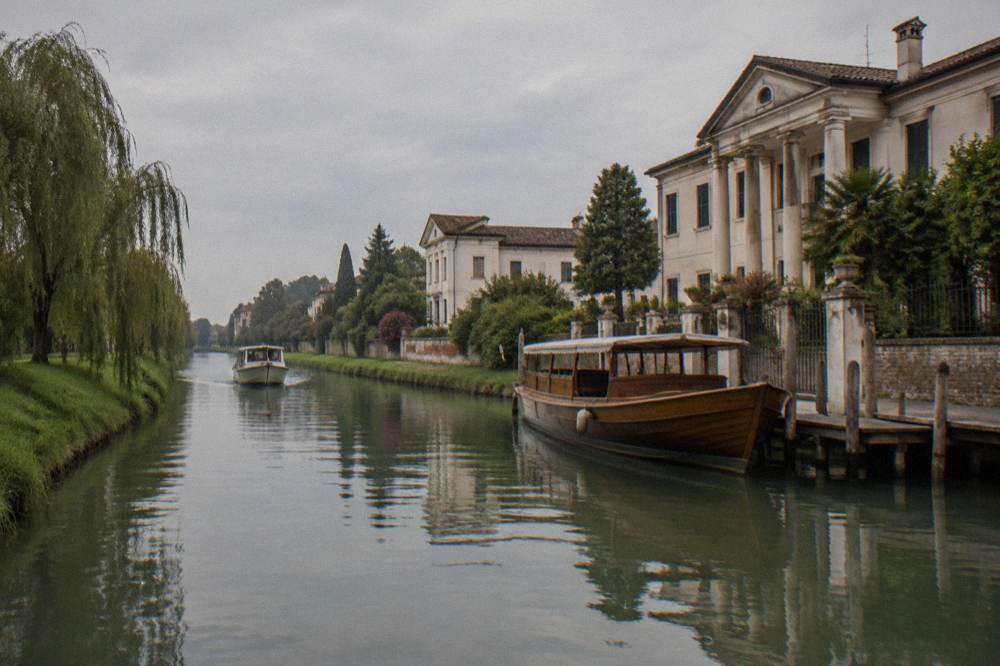 A long wooden passenger barge moored at a canal landing stage beside a villa wall