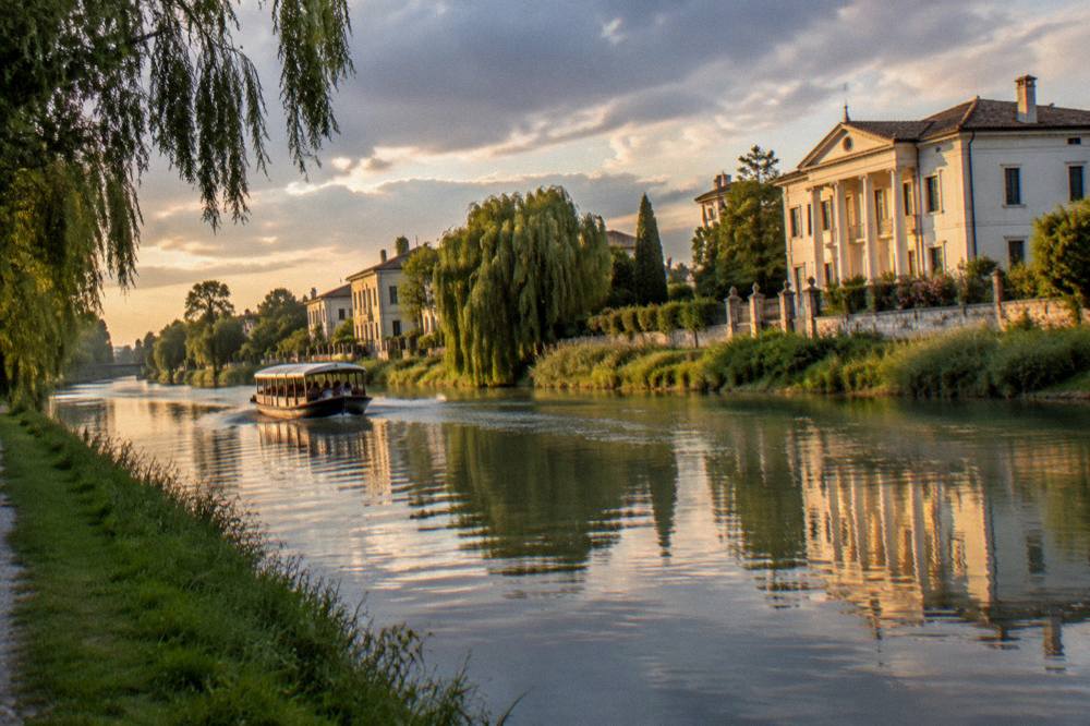 An evening view along a calm canal with villa facades lit on the far bank