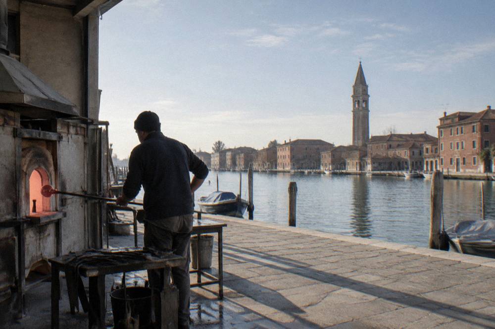A glassmaker shaping molten glass at a workshop furnace on the island of Murano