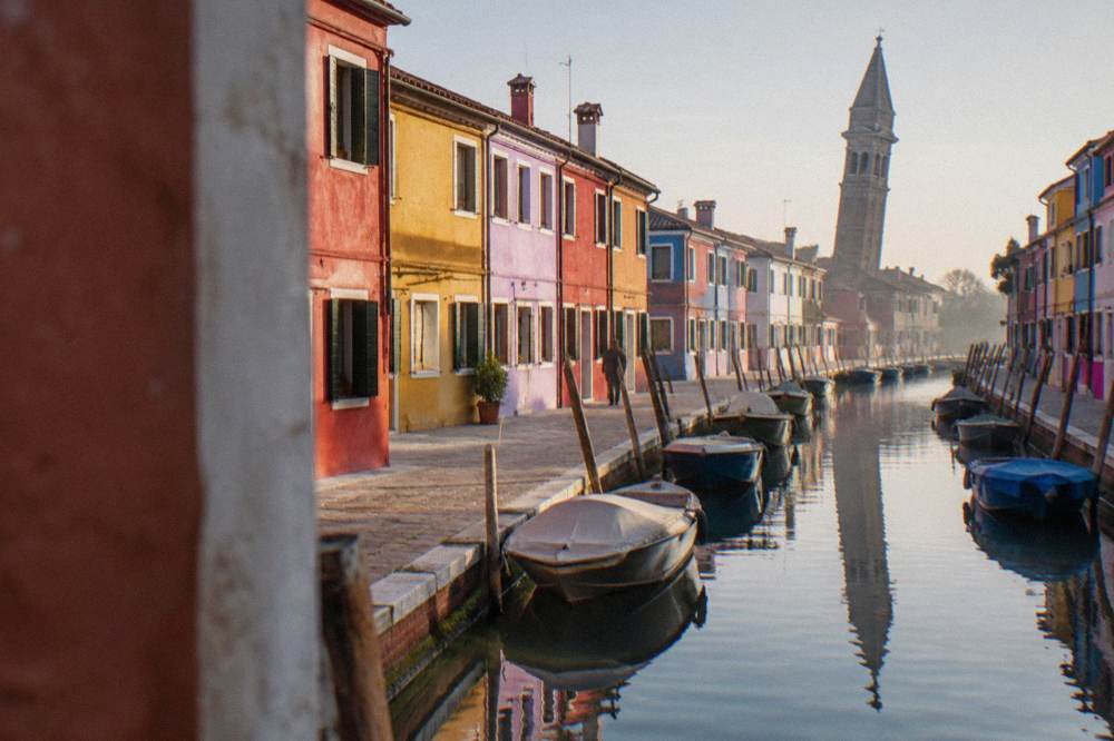 A quiet canal on Burano with brightly painted fishermen's houses reflected in the water